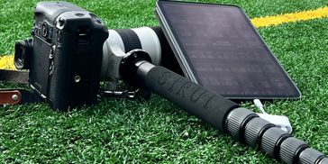 A professional camera with a long lens and an iPad on artificial grass.