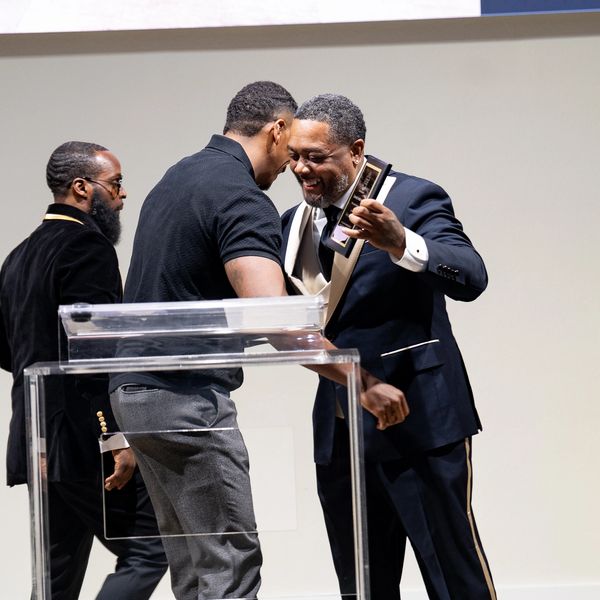 Two men warmly embrace on stage, one holding an award.