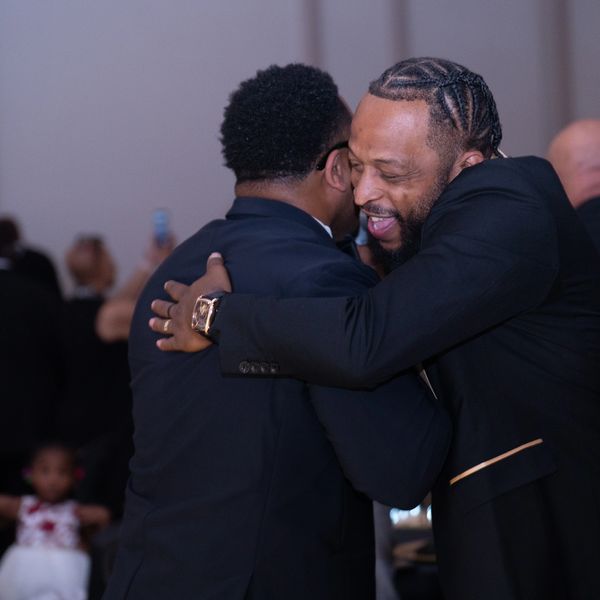 Two men warmly embrace in a joyful hug at an event.