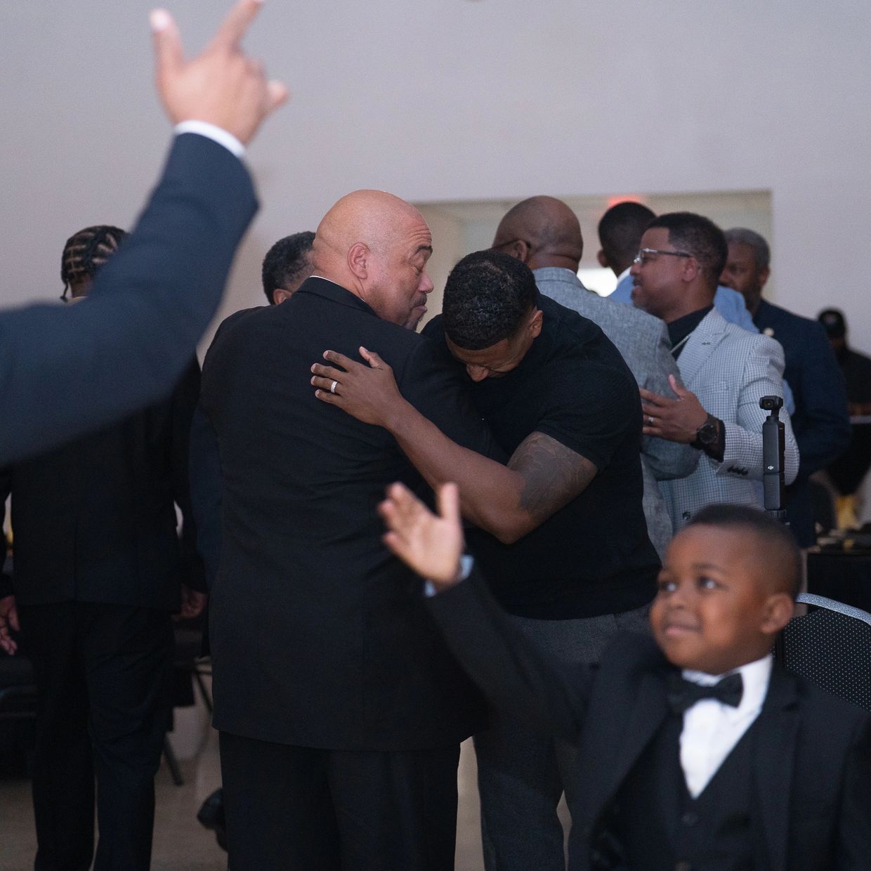Man hugging another man dressed in black suits at a formal event.