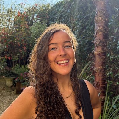 Smiling woman with curly hair standing outdoors in a garden.
