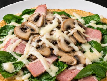 Pizza topped with mushrooms, spinach, ham, and melted cheese.