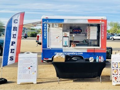 A colorful crepes food truck with a French flag banner and a black table in front.
