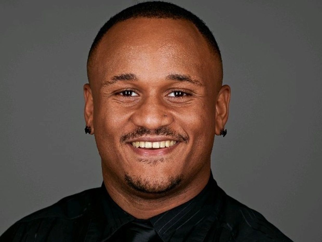 Smiling man in black shirt and tie against a gray background.