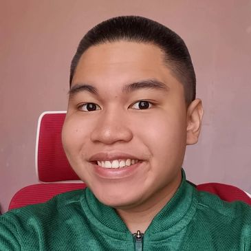 Young man smiling in a green jacket sitting on a red chair.