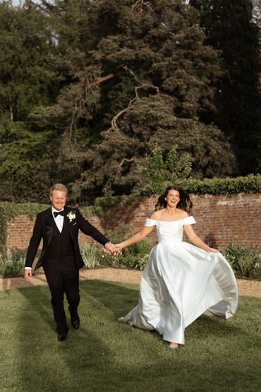 Newlywed couple joyfully running hand in hand outdoors on their wedding day.