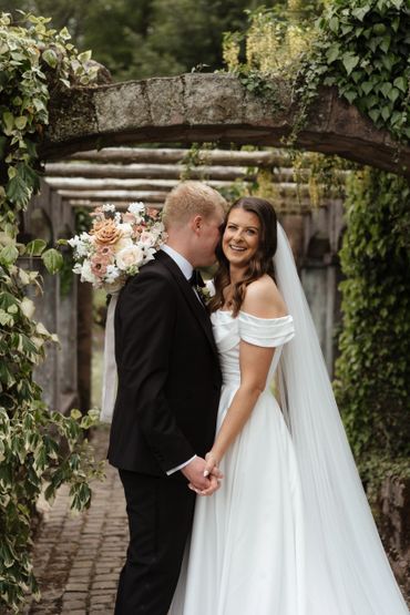 A bride and groom holding hands under a floral archway on their wedding day.