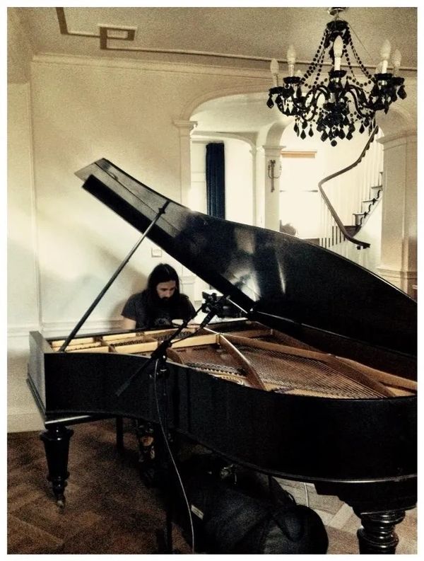 A person plays a grand piano in a vintage-style room with a chandelier.