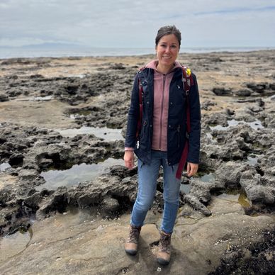 Woman standing on rocky shore wearing hiking boots.