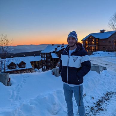 Smiling young man in winter clothes during sunset in snowy mountains.