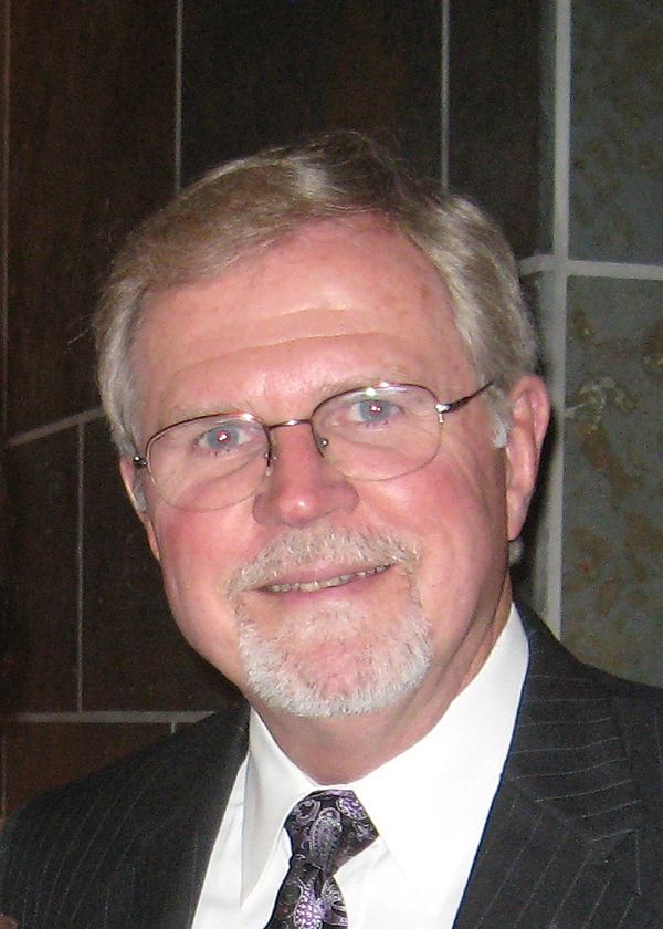 Smiling elderly man with glasses in a suit and tie.
