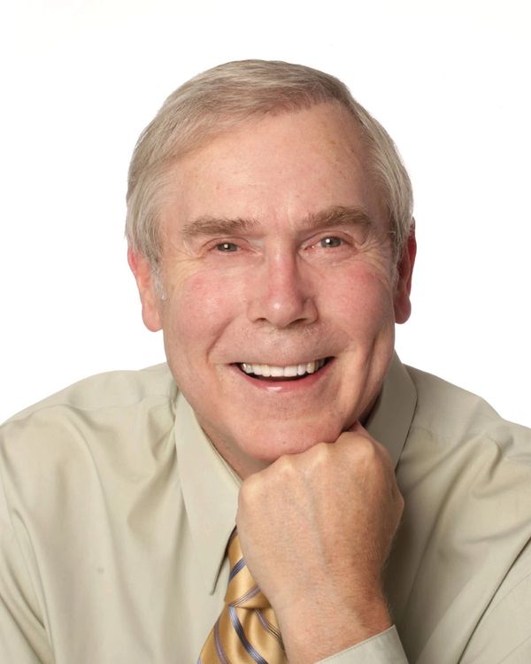 Smiling elderly man resting chin on hand in a beige shirt and striped tie.