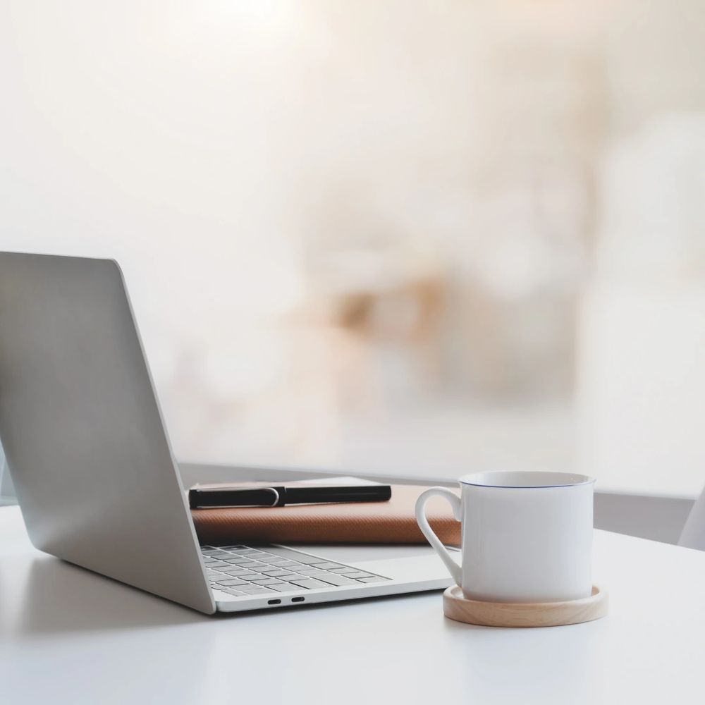 An open laptop on a table with a cup next to it on a coaster.