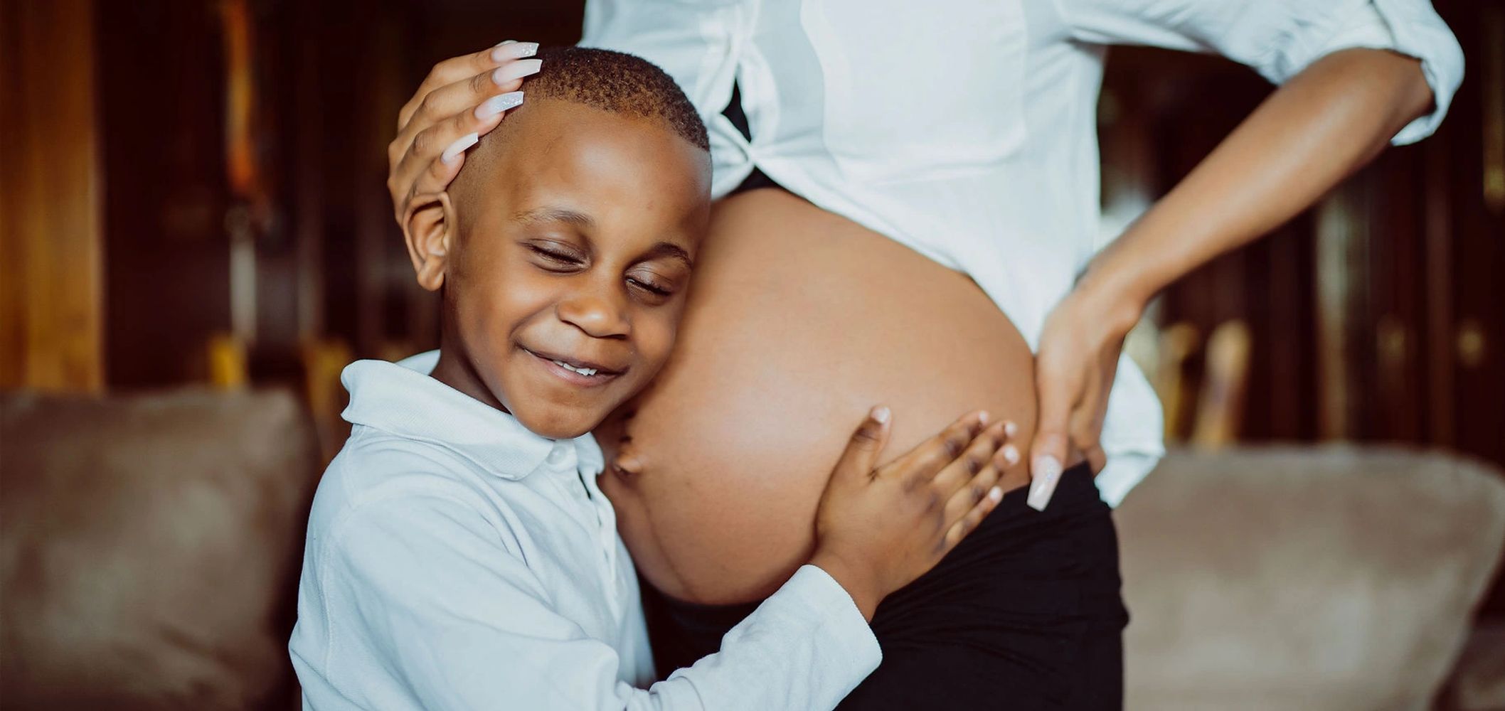 Young boy lovingly embraces his pregnant mother's belly.