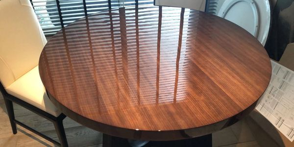 Shiny wooden round table reflecting window blinds.