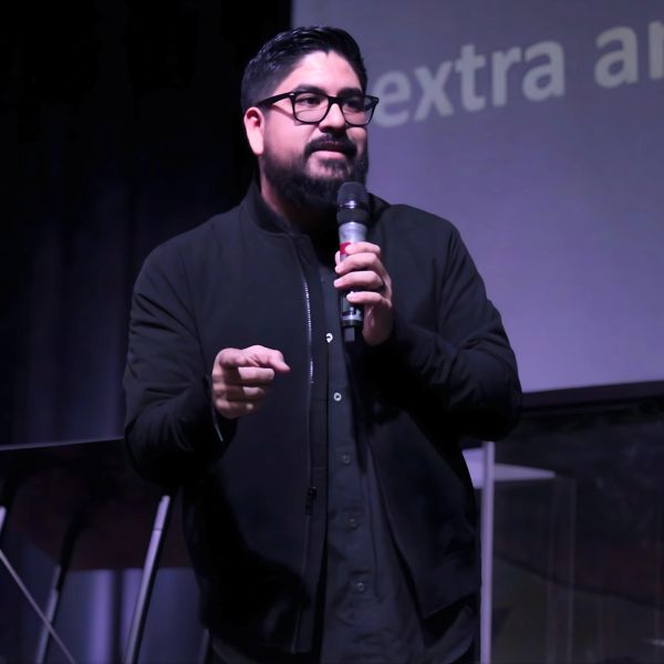 Man speaking on stage with a microphone in hand.