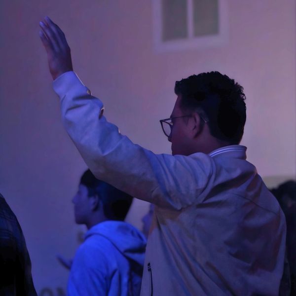 A person raising their hand in a dimly lit room with others around.