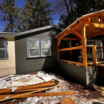 A cabin with a new wooden porch under construction in a snowy forest.