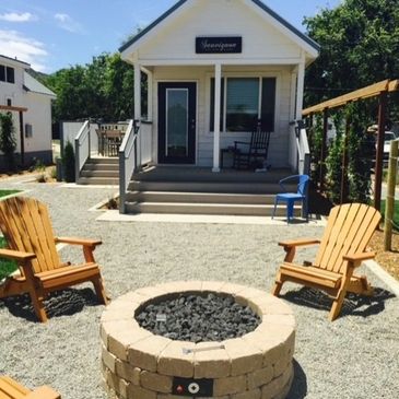 Cozy outdoor fire pit area with wooden chairs in front of a small white house.