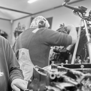 Two men working on motorcycle engines in a workshop.