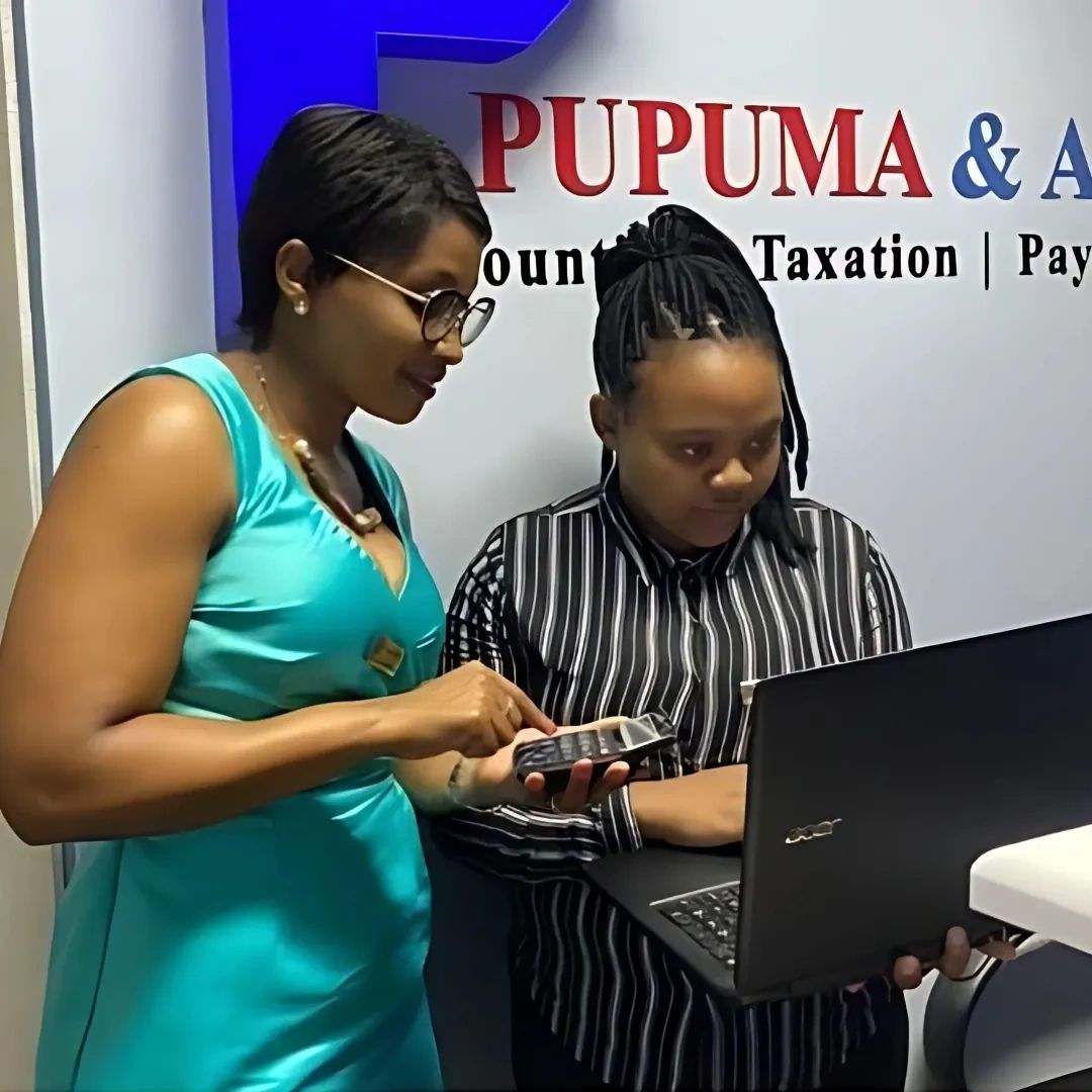 Two women collaborating on a laptop and calculator in an office setting.