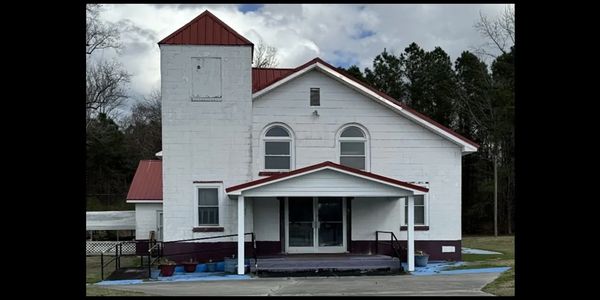 Old white church with a red roof and small porch in a wooded area.