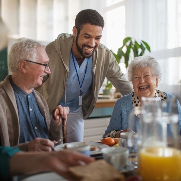A carer smiling with two elderly people sitting at a table