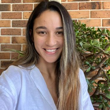 Smiling woman with long hair in white shirt against brick wall.
