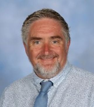 Smiling man in a light blue shirt and tie.