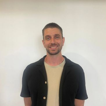 Smiling man standing against a plain white wall.