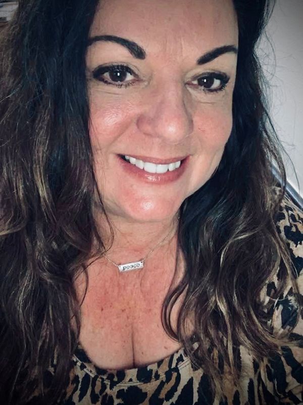 Smiling woman wearing a leopard print top and a "peace" necklace.