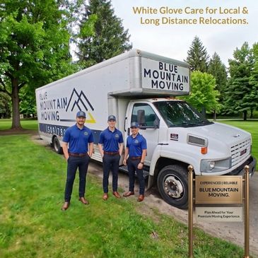 Three movers standing by a Blue Mountain Moving truck in a park area.