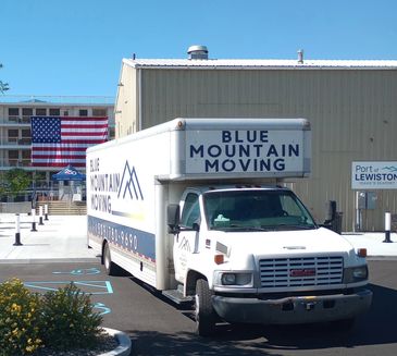 A Blue Mountain Moving truck parked near a building with an American flag.