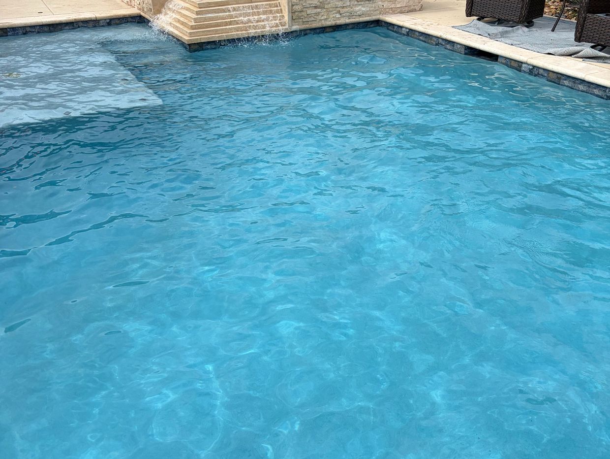 Clear blue swimming pool with a small waterfall feature and patio seating.