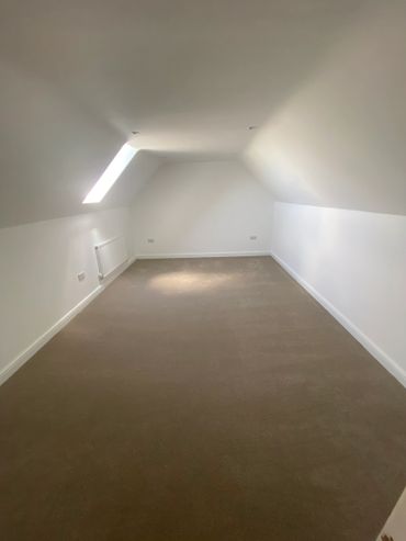 Empty attic room with slanted ceiling and skylight window.