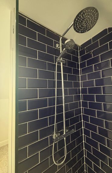 Modern shower with dual showerheads and dark subway tiles.