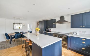 Modern kitchen with blue cabinets, white countertops, and a dining area with blue chairs.