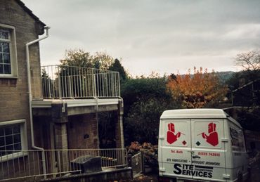 Service van parked near a house with metal railings and autumn foliage.