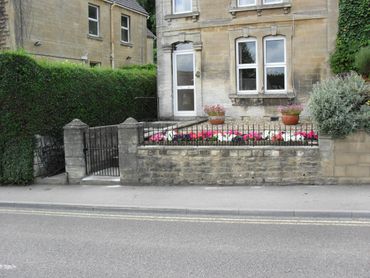 Stone house with flower garden and iron gate by the roadside.
