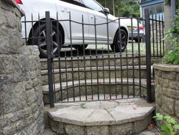 Black metal gate on stone steps with cars parked above.