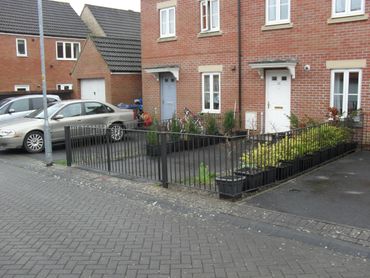 Residential brick houses with small fenced gardens and parked cars on a quiet street.
