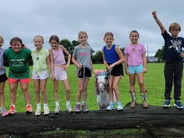 A group of children posing with a small llama outdoors.
