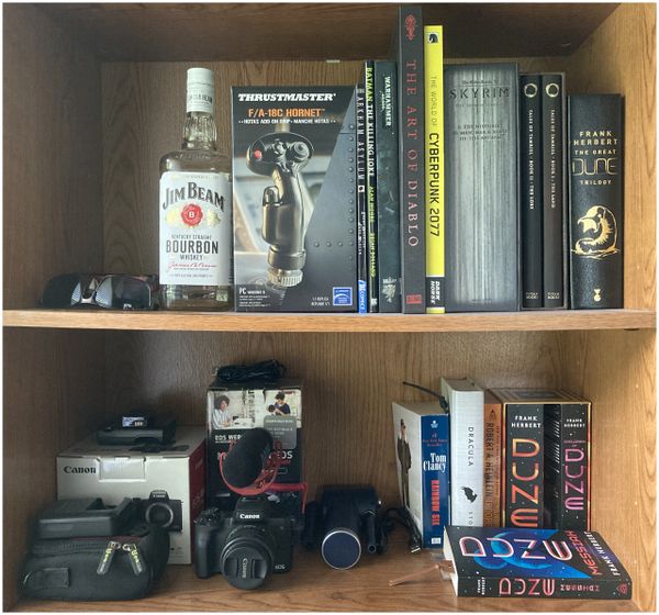 Books, a bourbon bottle, and camera equipment on wooden shelves.