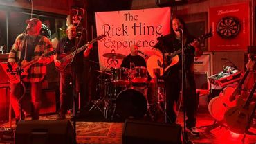 A four-member band performs live on a dimly lit stage with a banner behind them.