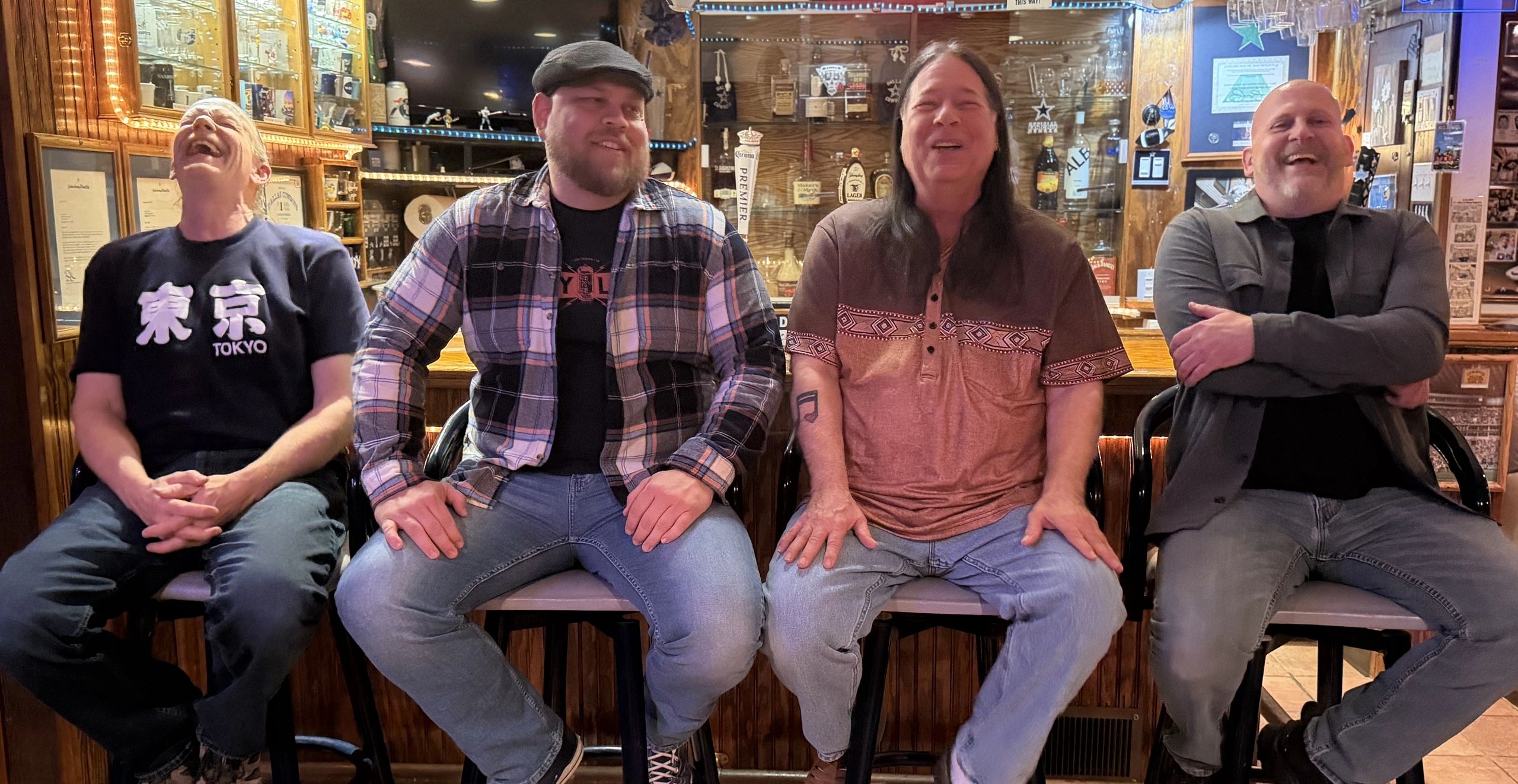 Four men laughing together while sitting on bar stools in a cozy bar.