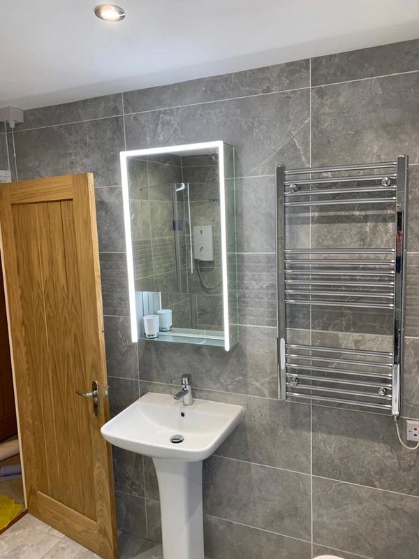 Bathroom setting; picturing a sink with LED mirror above. Large format grey marbled tiles