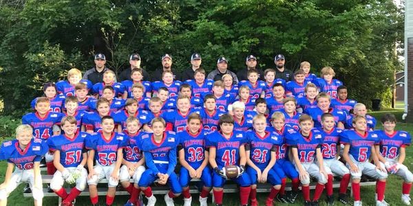 Youth football team in blue and red uniforms posing with coaches outdoors.