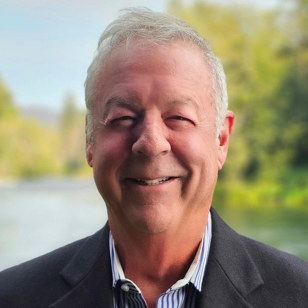 Smiling elderly man outdoors with blurred greenery background.