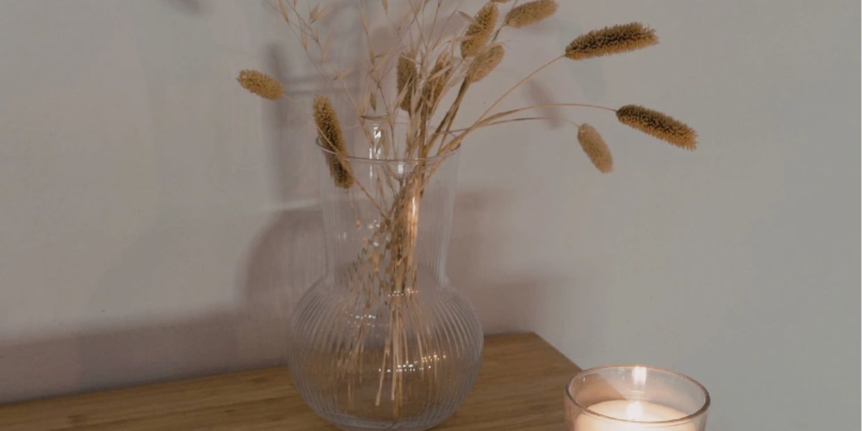 A cozy scene with a vase of dried flowers, a lit candle, and an open notebook with a pencil.