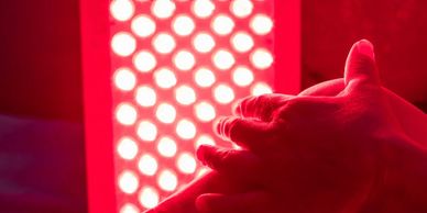 Hands placed in front of a red light therapy device with glowing LED lights